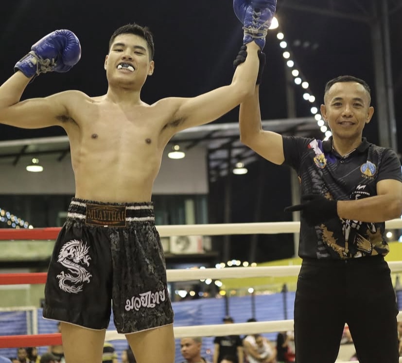 ภาพของนักมวยหนุ่มผู้ชนะ เทรนเนอร์ส่วนตัว ฟิตเนสกำลังยกมือขึ้นด้วยความดีใจหลังได้รับชัยชนะบนเวที พร้อ