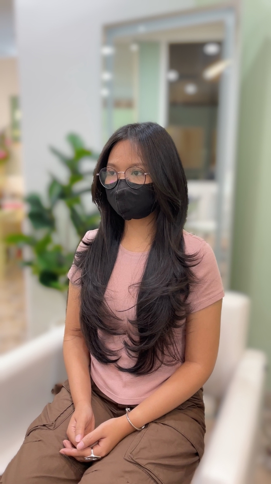 ตัดผมนอกสถานที่ ช่างตัดผมให้บริการตัดผมถึงที่บ้านหรือนอกสถานที่ ลูกค้านั่งรอในร้านทำผม เสื้อสีชมพู กางเกงสีน้ำตาล ทรงผมยาวสลวยสวยงาม พร้อมแว่นและหน้ากากอนามัย บริการตัดผมถึงบ้าน ตัดผมสวย ตัดผมตามสั่ง