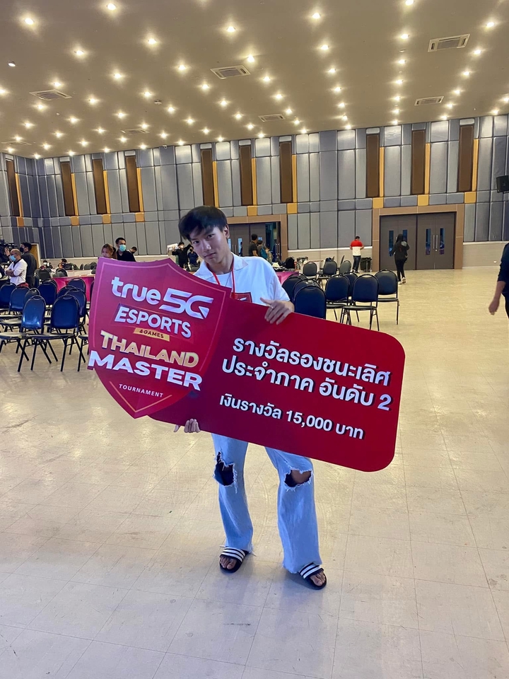 นักเล่นเกมหนุ่มถือป้ายประกาศผลรางวัลการแข่งขันอีสปอร์ตในงานแข่งเกม รับปั้มแรงค์ rov, บริการรับจ้างเล่นเกม, รับเล่นเกม rov, บริการปั้มดาว rov, รับไต่แรงค์เกม, รับปั้มแรงค์ฟีฟาย, รับปั้มแรงค์พับจี, รับดูแลไอดีเกม.