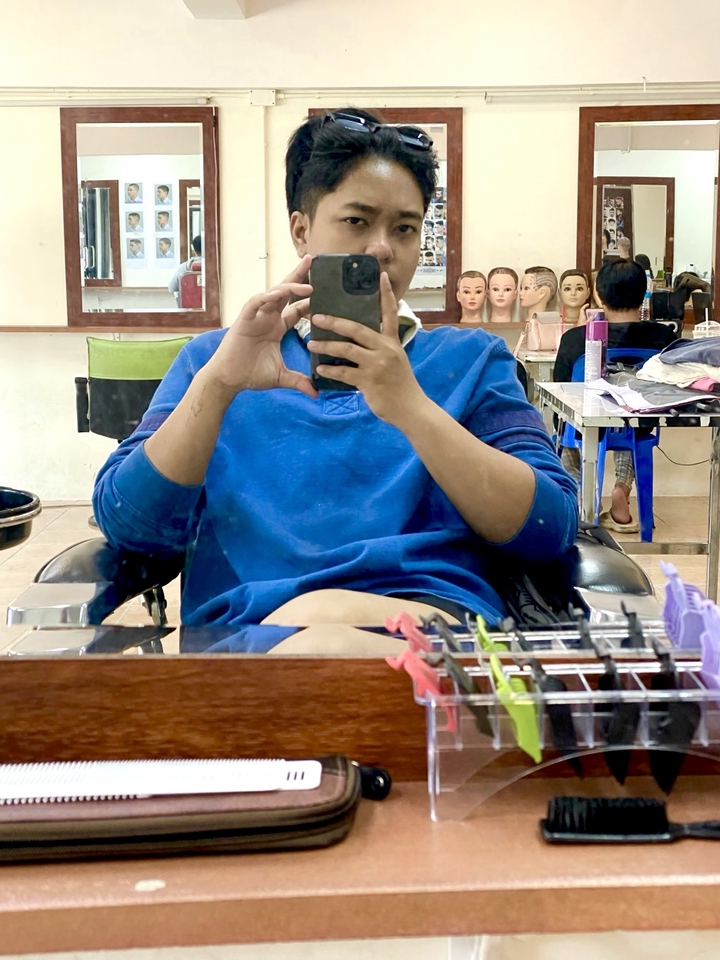 บริการตัดผมนอกสถานที่ ช่างตัดผมถ่ายเซลฟี่ในร้านทำผมพร้อมอุปกรณ์ตัดผม มองกระจกพร้อมโทรศัพท์ แสดงถึงบริการตัดผมเดลิเวอรี่ ช่างตัดผมที่บ้าน ราคาดี ตัดผมสวยถูกใจ ช่างทำผมใกล้ฉัน